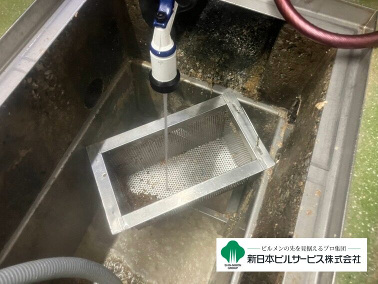 取り外したグリストラップ用バスケットを石鹸水で洗浄し、水で汚れを流している写真